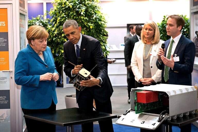 Space Tango cofounder Twyman Clements presenting a cube satellite to President Barack Obama and Chancellor Angela Merkel